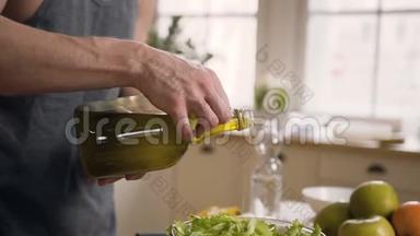 特写镜头。 年轻人把橄榄油倒在<strong>玻璃碗</strong>里，里面放着<strong>蔬菜</strong>，在家里准备新鲜沙拉